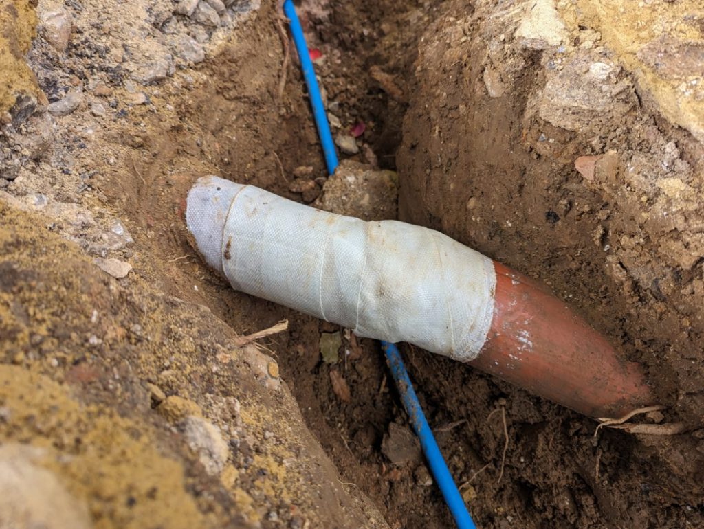 SylWrap HD Pipe Repair Bandage wrapped over a cracked underground clay drainage pipe