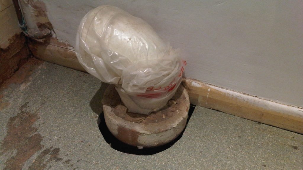 A large cracked area inadvertently left between a toilet waste pipe and a bathroom floor prior to undergoing repair