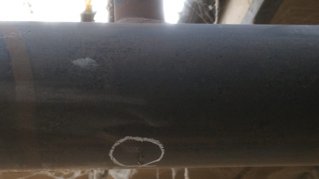 Pinhole leak underneath a tee section in a furniture factory sprinkler pipe system prior to undergoing repair
