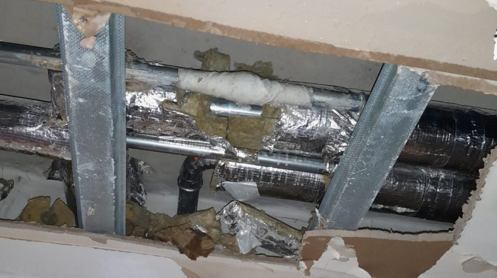 A steel pipe in a district heating system located in the roof of a building undergoes a live leak repair with a Sylmasta Pipe Repair Contractor Case